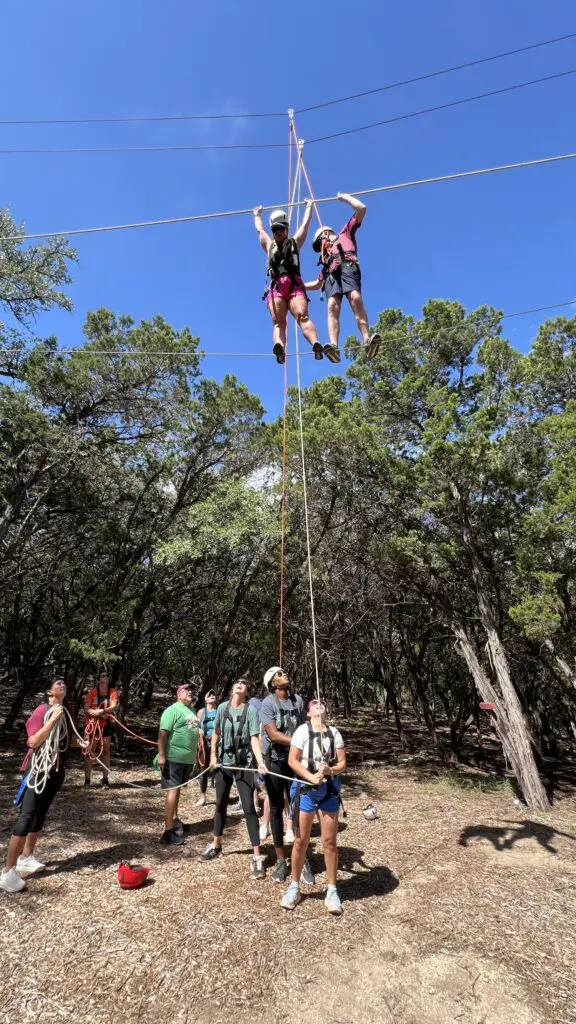 Two participants crossing cables while teammates coach from the ground at CVTC.